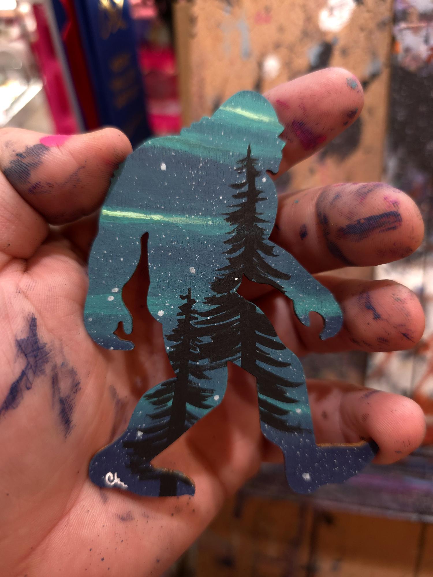 Blue hand-painted Sasquatch with pine trees and night sky